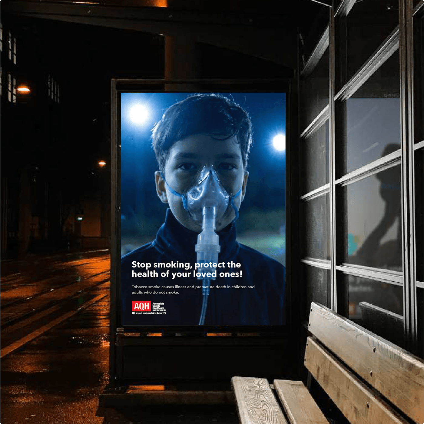 AQH-Wartehäuschen-Poster bei Nacht — dieselbe Passivrauch-Kampagne auf Straßenebene.